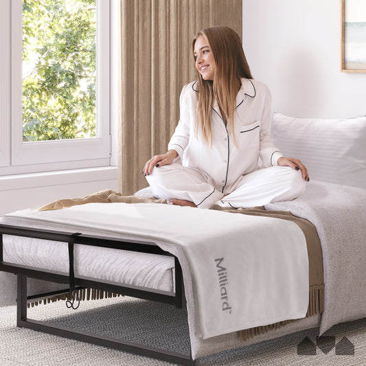 Smiling woman sitting on the Milliard Deluxe Presidential Folding Bed with mattress, pillow, and blanket